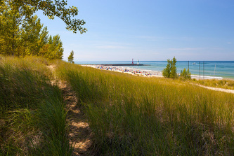 wide view from under tree looking out at Lake Michigan beach and pier with lighthouse