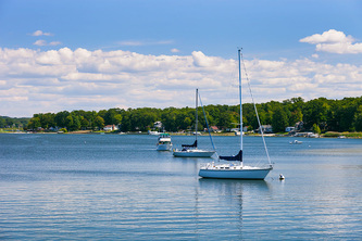 two sailboats and ski boat moored in harbor, trees and cottages on sunny day