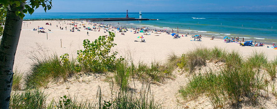wide view of sandy beach, pier and beach-goers on sunny day 